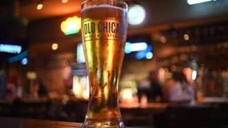 A tall glass of beer labeled Old Chicago, inside a bar. | Wirestock | Dreamstime.com