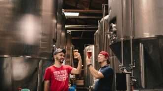 Two men holding full beer glasses up amid tall stainless steel tanks in a brewery. | Photo by <a href=%40elevatebeer1591.html on <a href=brewery0a0b.html
				/></noscript>
			</picture>
		</div>
					</a>
					</div>
		<div class=